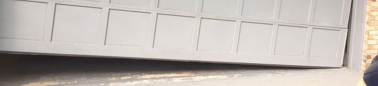 Close-up of dented and misaligned steel garage door panel before repair in Brooklyn Park
